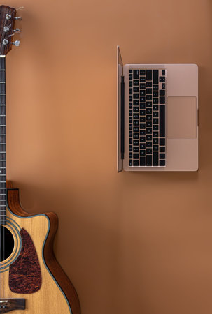 Acoustic guitar and laptop on a brown background, top view, copy space.