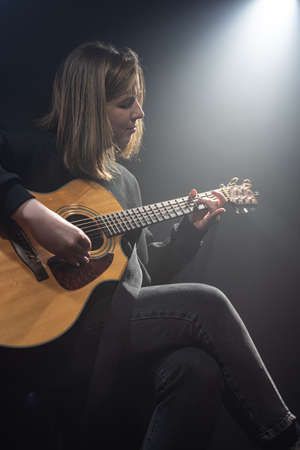 Young woman playing acoustic guitar in a dark room with haze.の写真素材