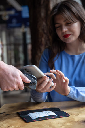 Paypass, male hands holding black pos terminal and female brings smartphone.