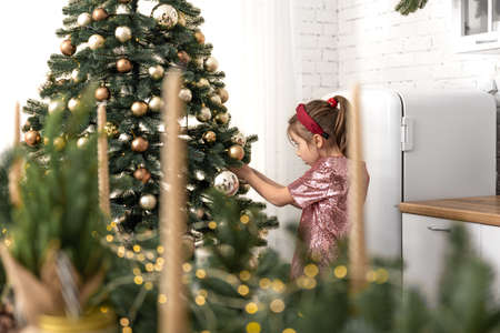 A little girl decorates a Christmas tree, hangs balls.の写真素材
