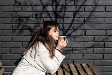 Young woman enjoying a drink against the brick wall of the coffee shop exterior.の写真素材