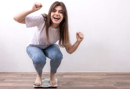Happy girl is weighed on the scales at home, the joy of losing weight.の写真素材