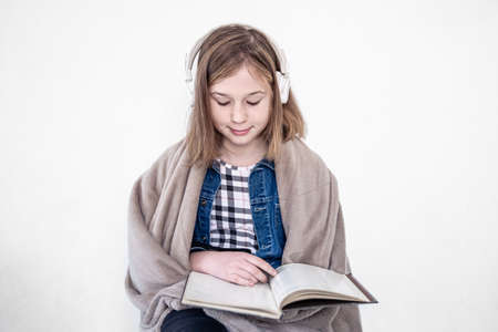 Teenage girl in headphones and with a book in her hands on a white background.の写真素材