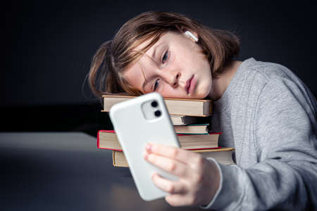 A little girl sits near books and takes a selfie, bored from reading.の写真素材