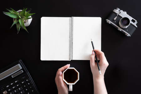 Female hands and blank notepad on black background, flat lay.の写真素材