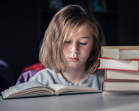 Serious little girl reading a book sitting at the table.の写真素材