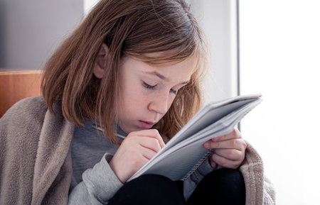 Close-up, a little girl draws in a notebook, wrapped in a plaid.