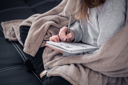 Close-up, a little girl draws in a notebook, wrapped in a plaid.の写真素材