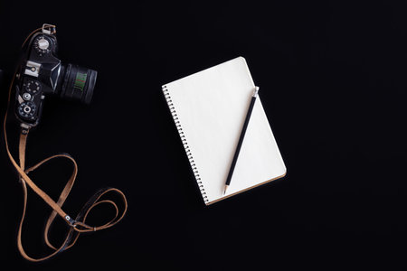Vintage retro camera and notepad on black background, flat lay.