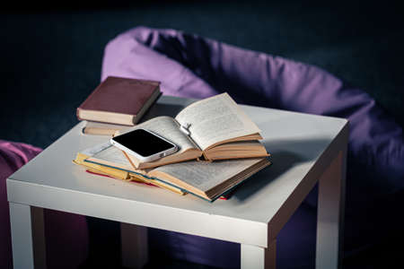 Books on a small white table on a blurred background of the interior with poufs.の写真素材