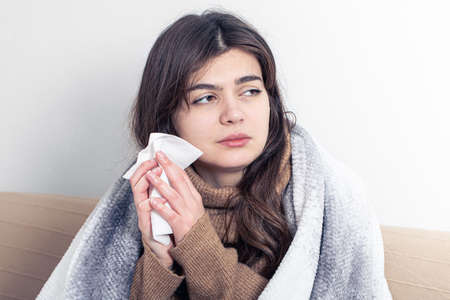 A sick young woman at home on the sofa with a cold.の写真素材