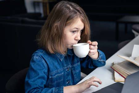 Tired girl in front of a laptop with a cup of tea and books.の写真素材