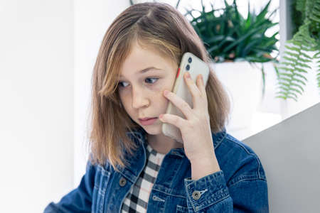 Cute little girl in a denim shirt talking on the phone with a surprised face.の写真素材
