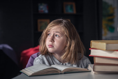 Serious little girl reading a book sitting at the table.
