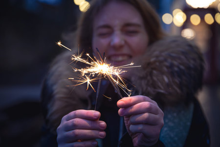 Burning sparklers in the hands of a young woman in the dark.