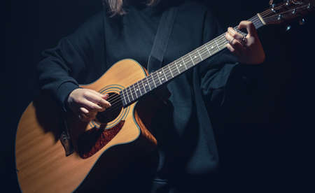 A young woman with an acoustic guitar in the dark under a ray of light.の写真素材