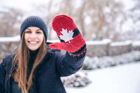Happy young woman in red mittens with the flag of Canada in snowy weather.の写真素材