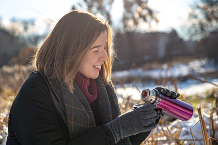A young woman enjoys a hot drink from a thermos on a walk in winter.