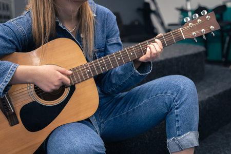 Close-up, a woman in a denim suit plays the guitar.