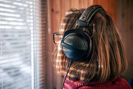 A woman with headphones looks through the blinds at the early morning sunlight.の写真素材