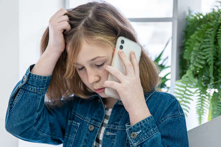 Cute little girl in a denim shirt talking on the phone.の写真素材