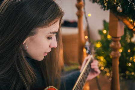A young woman playing guitar sitting on the steps at home.の写真素材