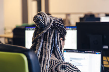 Close-up of dreadlocks of a girl working at the computer, back view.
