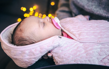 Newborn baby girl with pacifier on blurred background with bokeh.