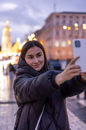 A woman takes a photo on the background of the night city on a smartphone.
