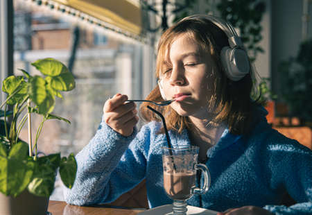 Little girl listens to music in headphones and drinks cocoa with sunny morning.の写真素材