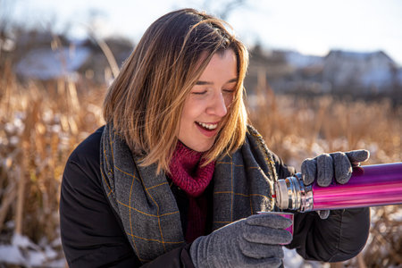 A young woman enjoys a hot drink from a flask on a walk in winter.