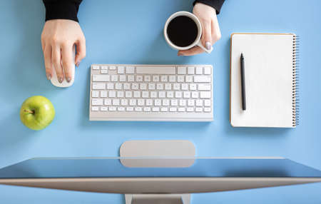 Top view, female hands work at the computer, blue background.の写真素材