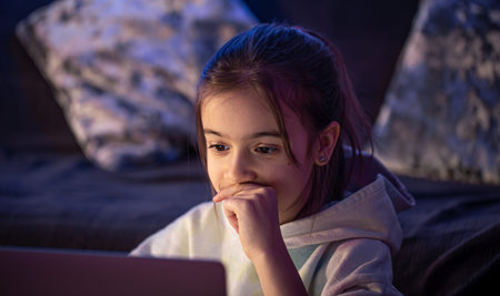 A little girl uses a laptop late at night.