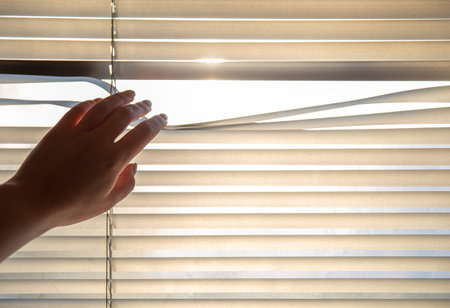 Womans hand taking a peak through the window blinds.