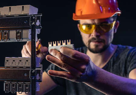 A male electrician works in a switchboard with an electrical connecting cable.の写真素材