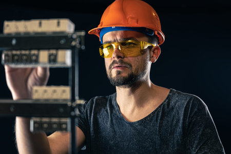 A male electrician works in a switchboard with an electrical connecting cable.