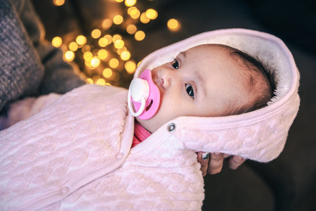 Newborn baby girl with pacifier on blurred background with bokeh.