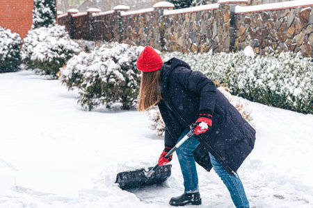 Young woman cleans snow in the yard in snowy weather.