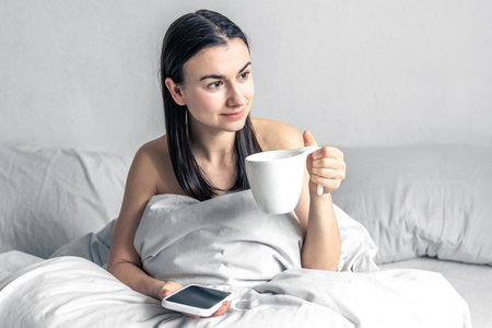 Young woman with a smartphone and a cup of coffee in her hands.