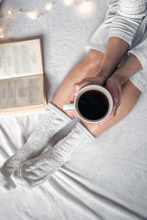 Cup of coffee in female hands in bed, top view.の写真素材