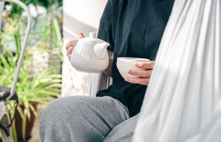 A white cup of tea and a teapot in a womans hands.の写真素材