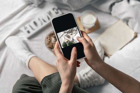 A woman takes a picture of her breakfast while lying in bed.の写真素材