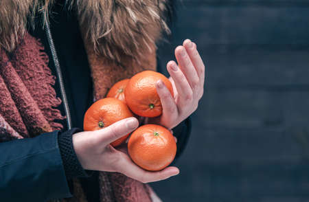 Close-up of tangerines in female hands on a blurred background.の写真素材