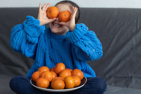 A little girl with tangerines at home on the sofa.の写真素材