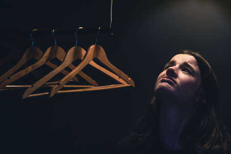A young woman near empty hangers in the dark under a lamp.の写真素材