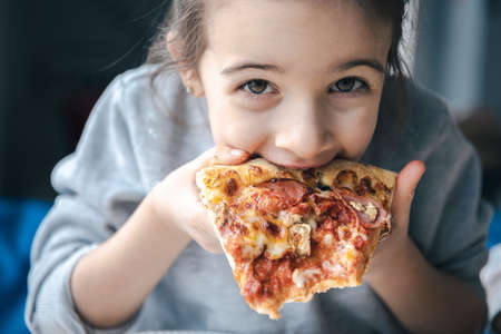 Portrait of a little girl with an appetizing piece of pizza.の写真素材