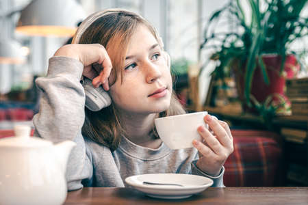 A little girl in headphones in a cafe with a cup of tea.の写真素材