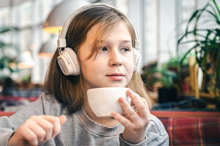 A little girl in headphones in a cafe with a cup of tea.の写真素材