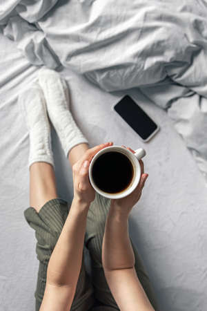 Cup of coffee in bed in female hands, top view.の写真素材