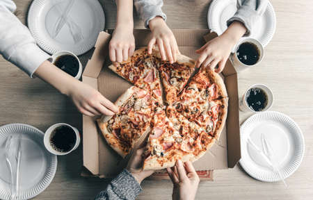 Young people taking slices of hot pizza from cardboard box at table, top view. Food delivery service.の写真素材